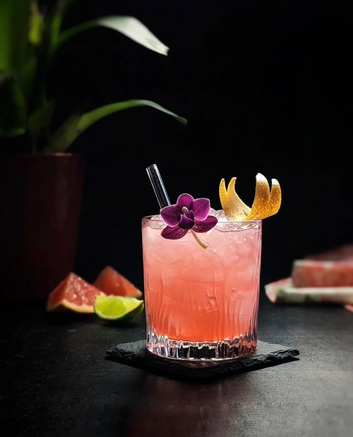 Pink cocktail garnished with a purple orchid and citrus twist.